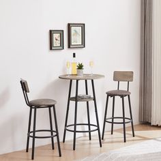 two stools and a table in a room with white walls, hardwood floors and pictures on the wall