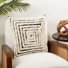 a white chair with a black and white pillow on it next to a potted plant