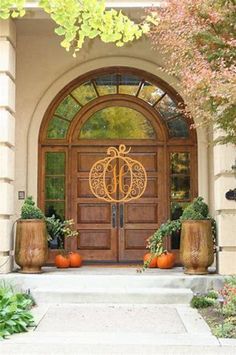 the front door is decorated with pumpkins and potted plants in large planters