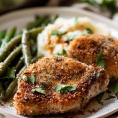 two pieces of chicken on a plate with green beans and mashed potatoes