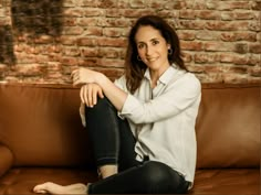 a woman sitting on top of a brown couch next to a brick wall and floor