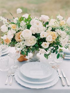 a table set with white plates, silverware and flowers