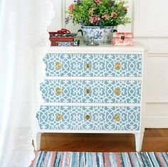 a blue and white chest of drawers with gold knobs on the top, in front of a window