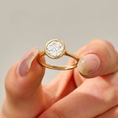 a woman's hand holding a gold ring with a diamond in the middle and a white background