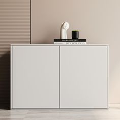 a white cabinet sitting next to a vase on top of a wooden floor in front of a beige wall