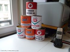 several cans of oil are stacked on top of each other next to a cell phone