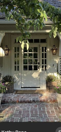 the front door to a home with potted plants and flowers on the brick walkway