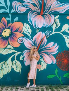 a woman standing in front of a colorful wall with flowers painted on it and wearing sunglasses