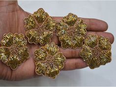 four gold flower shaped brooches in the palm of someone's hand