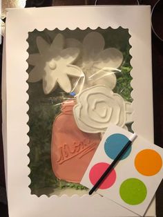 there is a cookie in the shape of a jar with flowers on it and a paintbrush next to it