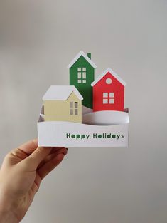 someone is holding up a card that says happy holidays in front of some small houses