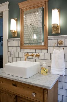 a white sink sitting under a bathroom mirror next to a wooden cabinet and counter top