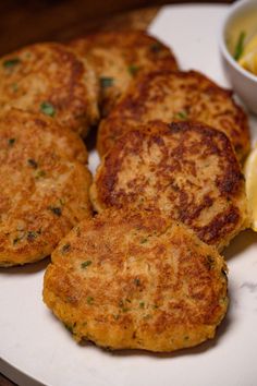 four crab cakes on a plate next to a bowl of lemon wedges and salad