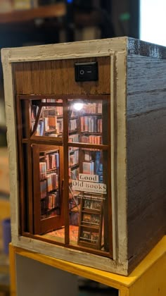 a display case with books in it on top of a wooden table next to a window