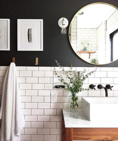 a bathroom with black walls and white tiles on the wall, two round mirrors above the sink