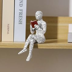 a white statue sitting on top of a wooden shelf holding a red book in its hands