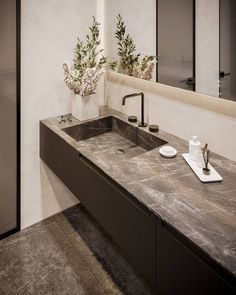 a bathroom sink sitting under a mirror next to a vase with flowers on it's side