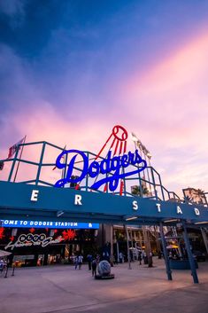 people are walking under a neon sign at the entrance to dodger's stadium