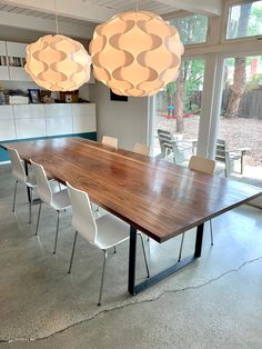 a large wooden table with white chairs and lights hanging from it's ceiling in an open room