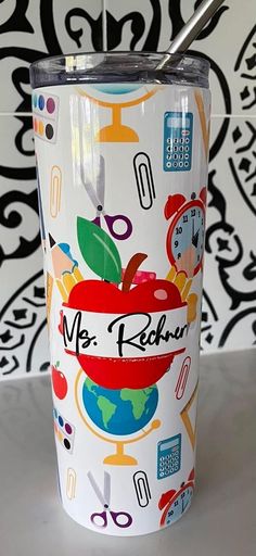 a travel mug with an apple and scissors on the side, next to a wallpaper