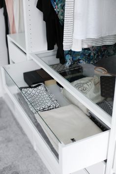 an open drawer in a closet with clothes on hangers and other items sitting on the shelves