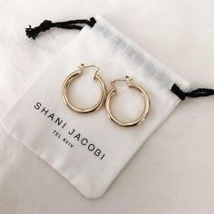 two pairs of gold hoop earrings sitting on top of a white bag