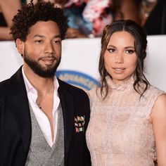 a man and woman standing next to each other on a red carpet with people in the background