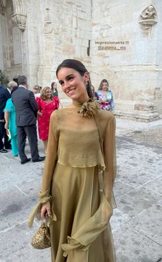 a woman standing in front of a building wearing a tan dress and holding a purse