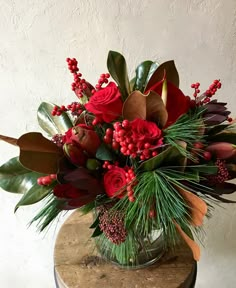 a vase filled with red flowers and greenery on top of a wooden table next to a wall