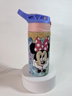 a cup with a minnie mouse design on it and a blue lid sitting on a stand