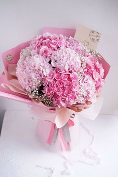 a bouquet of pink flowers is sitting on a white surface with a note attached to it