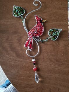 a red bird hanging from a wire on top of a wooden table next to a piece of glass