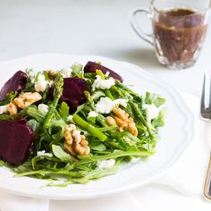 a salad with beets, goat cheese and walnuts on a white plate next to a cup of coffee