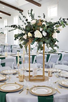 a centerpiece with white flowers and greenery on a table in a banquet hall