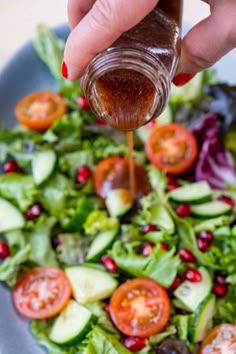 someone pouring dressing into a salad with lettuce, tomatoes and cucumbers