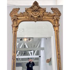 a man taking a selfie in front of a large gold mirror with an ornate frame