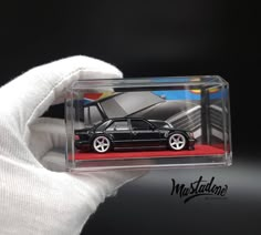 a miniature model of a black car in a clear case with red carpet and white gloves