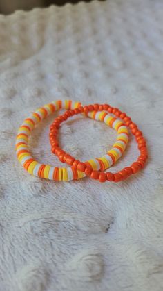 two orange and yellow bracelets sitting on top of a white blanket