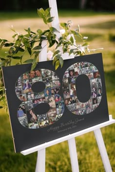 a white easel holding a sign with photos and greenery in the shape of an 80