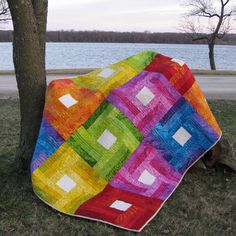 a multicolored quilt on the ground next to a tree and water in the background