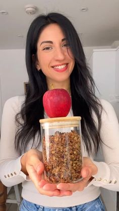 a woman holding an apple and granola in a jar