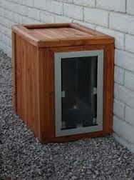 a wooden box with a cat in it sitting on the ground next to a brick wall