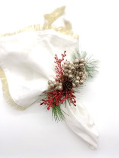 a white napkin with red berries and pine cones on it next to a christmas decoration