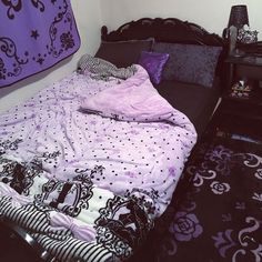 an unmade bed with purple and black comforter on it, next to a night stand