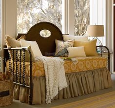 a bed sitting in the middle of a living room next to a window filled with lots of pillows