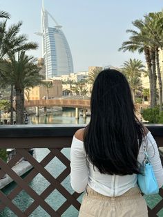 a woman standing on a bridge looking at the water and palm trees in front of her