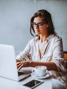 a woman sitting at a table with a laptop computer in front of her and a cup of coffee