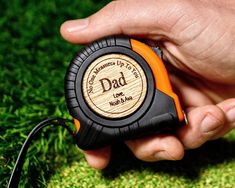 a hand holding a tape measure with the words dad engraved on it, in front of some green grass