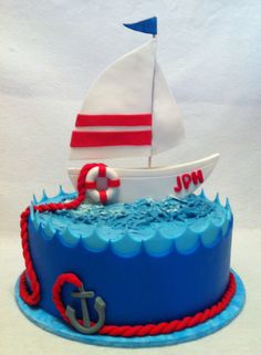 a blue cake with a sailboat on top and an anchor in the middle is sitting on a white surface