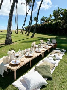 a long wooden table with plates and place settings on it in front of palm trees